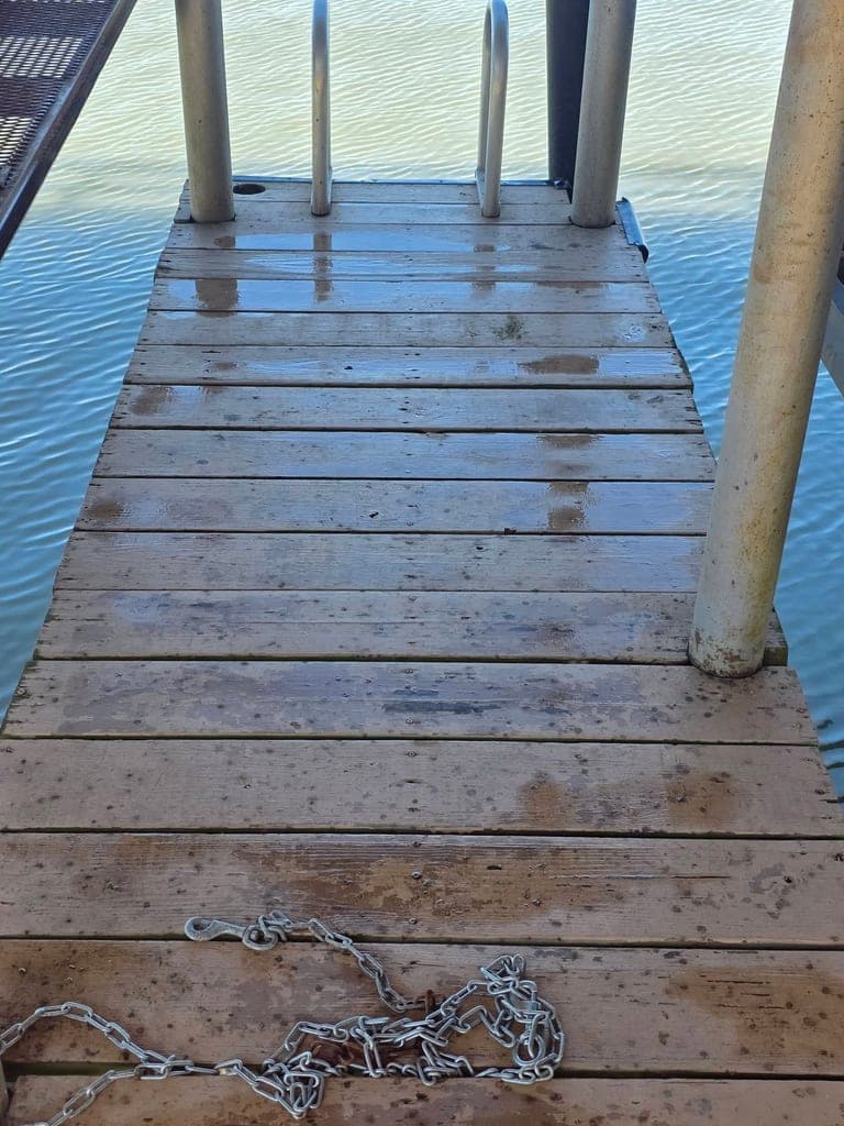 Wet wooden dock ramp with boat chain, freshly washed over lake water