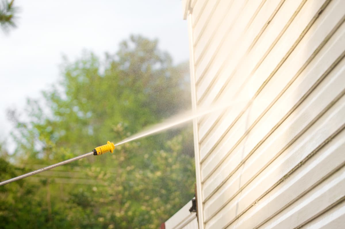 Pressure washer spraying siding clean during a house wash